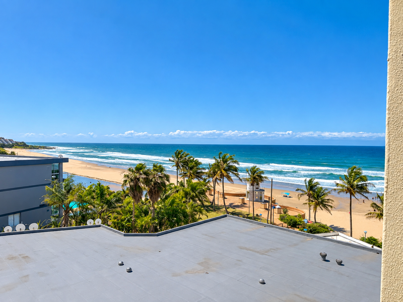 A clear, elevated view overlooking the beach, ocean, and coastal landscape from an apartment balcony.