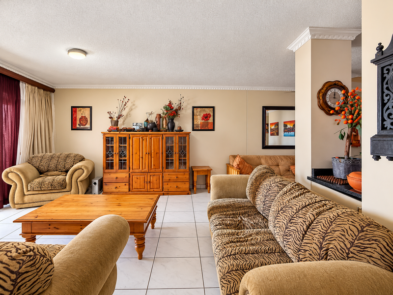 A spacious living room featuring neutral tiled flooring, crown molding, and a convenient built-in breakfast bar connecting to the adjacent kitchen area.