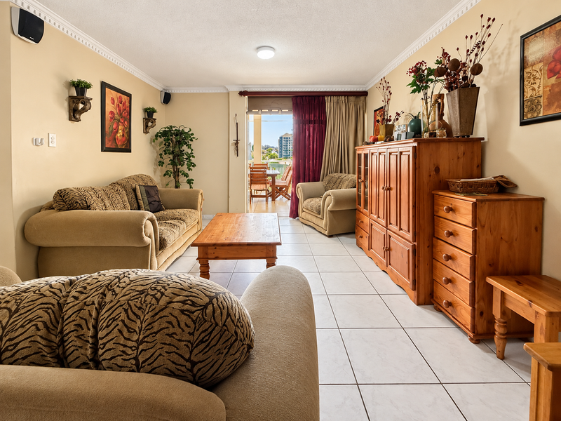 A spacious living room featuring tiled flooring and crown molding, with direct access to an outdoor balcony area.