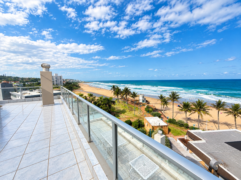 Spacious balcony featuring tiled flooring and a glass balustrade, offering expansive panoramic views of the coastline and beach.