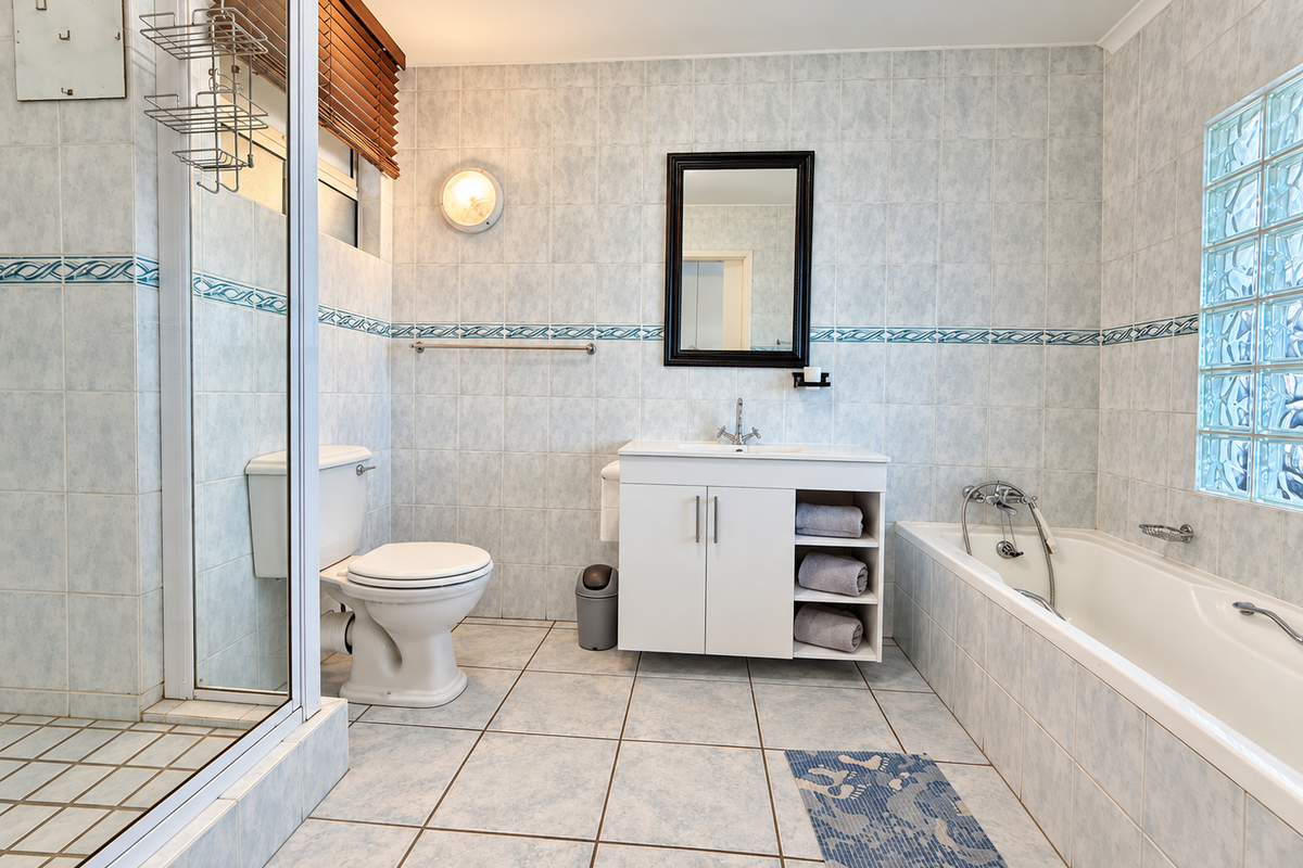 A functional bathroom featuring a separate shower, bathtub, vanity cabinet, and tiled finishes with a glass block window for natural light.