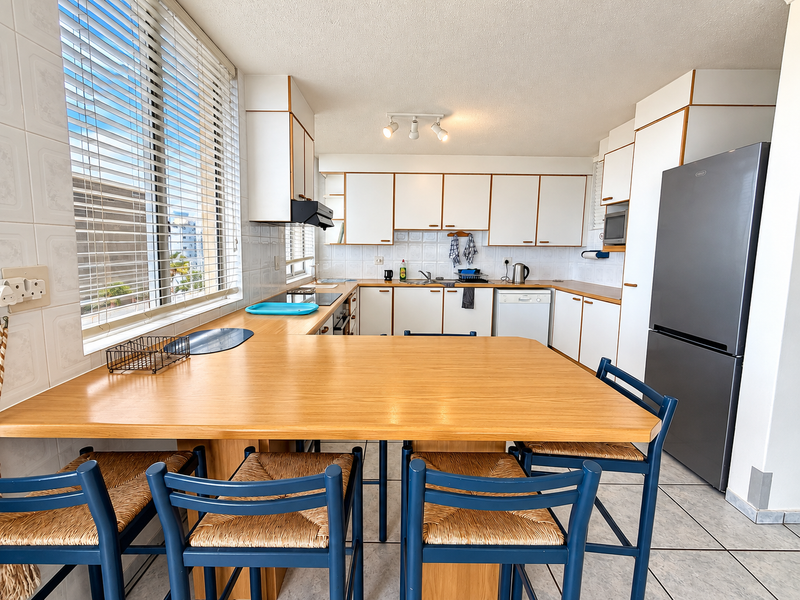 A functional kitchen featuring white cabinetry, laminate countertops, a built-in breakfast bar, and tiled flooring, offering a bright and practical workspace.