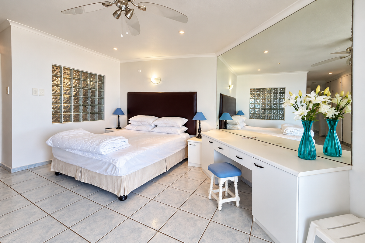 Spacious bedroom featuring tiled flooring, a built-in vanity with a large wall mirror, and a unique glass block window feature.