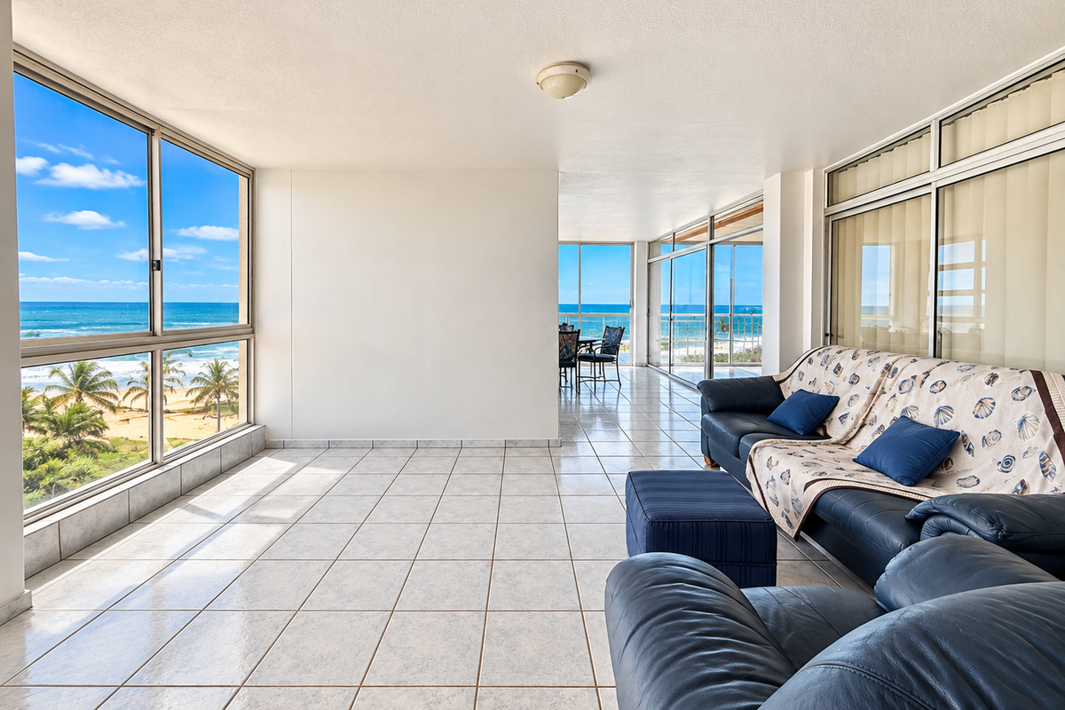 Spacious sunroom or living area featuring large windows with panoramic ocean views, tiled flooring, and direct access to an outdoor balcony space.
