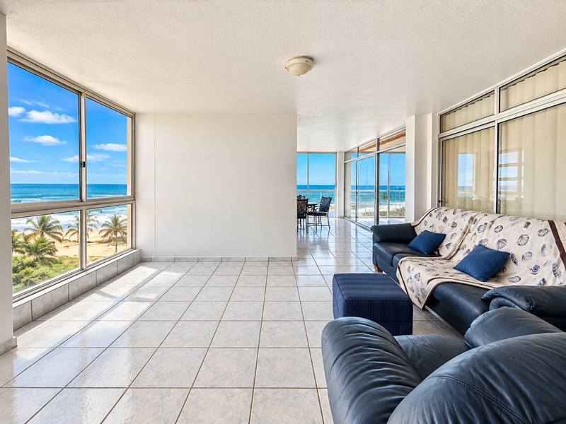 Spacious sunroom or living area featuring large windows with panoramic ocean views, tiled flooring, and direct access to an outdoor balcony space.