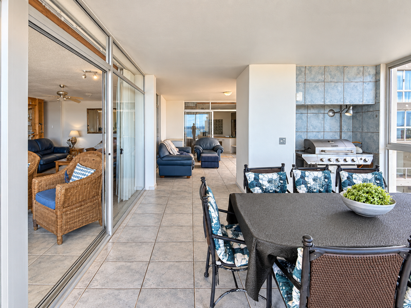 Spacious covered balcony featuring tiled flooring, sliding glass doors, and a built-in barbecue area, perfect for outdoor dining and entertaining.