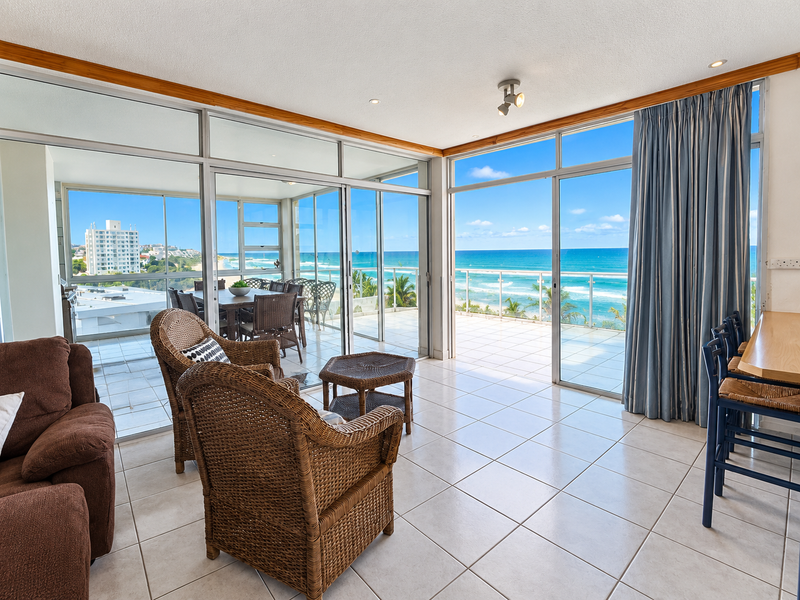 Spacious open-plan living area featuring large sliding glass doors that open onto a balcony with expansive ocean views and tiled flooring throughout.