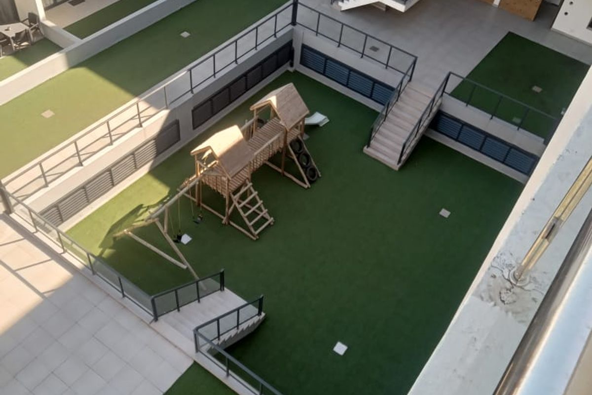 An elevated view of the apartment complex courtyard featuring a landscaped artificial lawn, playground area, and modern staircases with metal railings.
