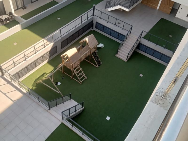 An elevated view of the apartment complex courtyard featuring a landscaped artificial lawn, playground area, and modern staircases with metal railings.