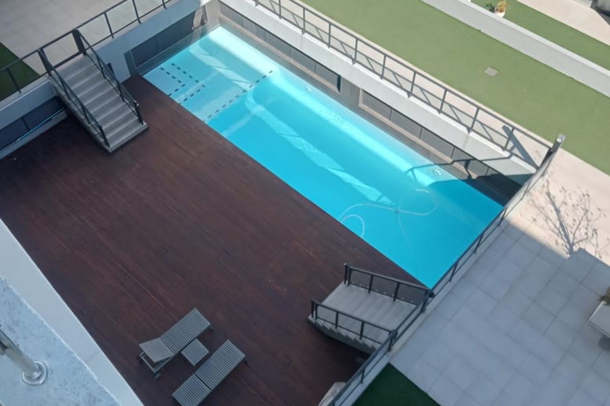 An elevated view of a modern apartment complex courtyard featuring a swimming pool, timber decking, and landscaped artificial lawn areas.