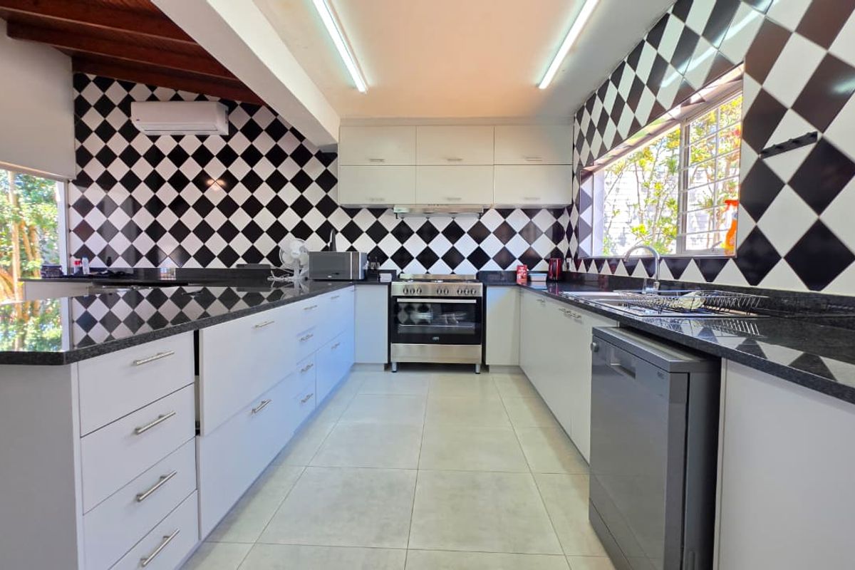 Modern kitchen featuring granite countertops, built-in oven, extractor fan, and a distinctive black and white diamond-patterned tiled backsplash with exposed timber ceiling beams.