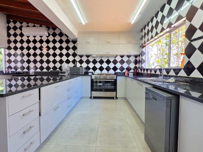 Modern kitchen featuring granite countertops, built-in oven, extractor fan, and a distinctive black and white diamond-patterned tiled backsplash with exposed timber ceiling beams.