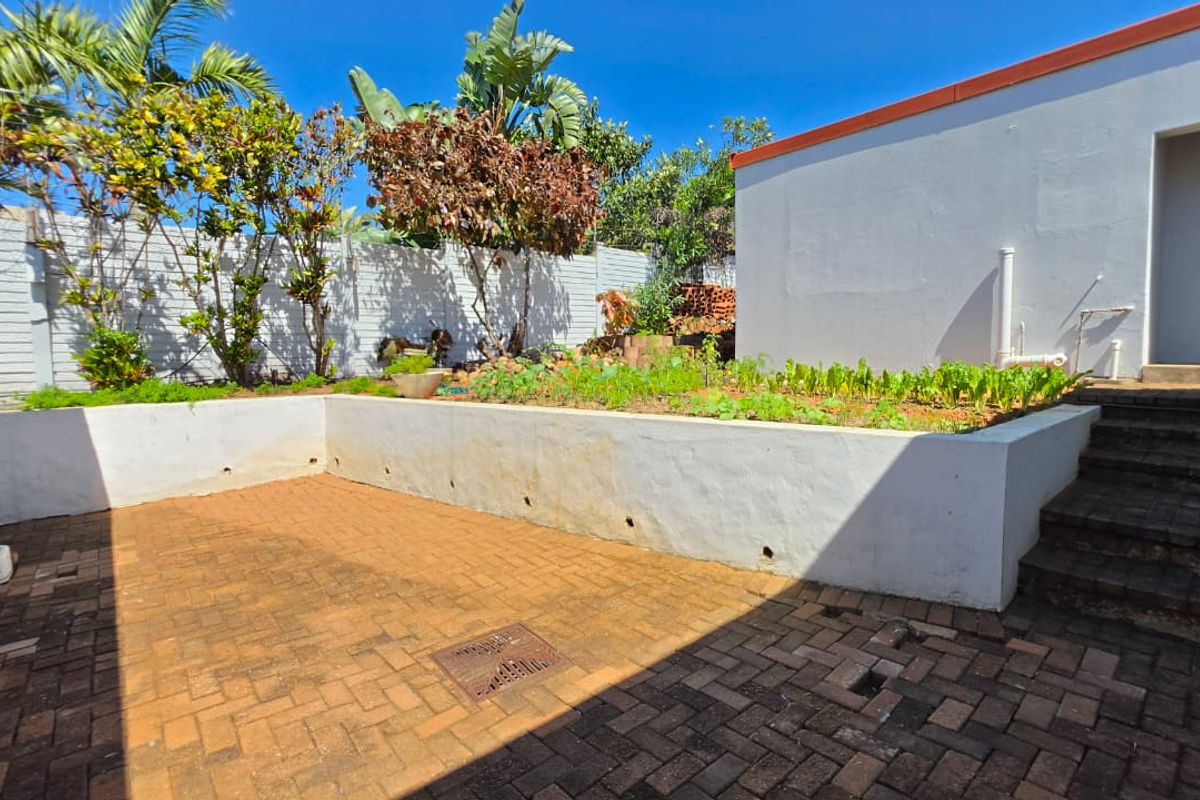 Rear courtyard area featuring a raised garden bed, brick paving, and concrete steps leading to the building entrance.