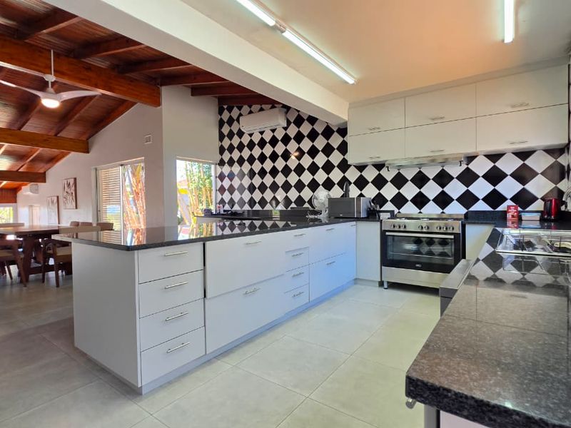 Spacious open-plan kitchen featuring a large island, granite countertops, and modern cabinetry, seamlessly flowing into the dining area under exposed timber ceiling beams.