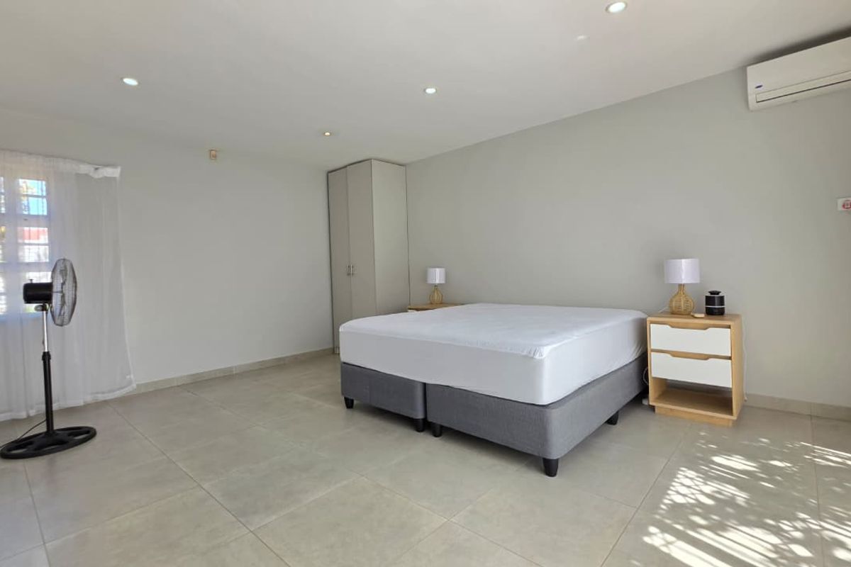 Spacious bedroom featuring neutral tiled flooring, recessed downlighting, a built-in wardrobe, and a wall-mounted split-system air conditioning unit.