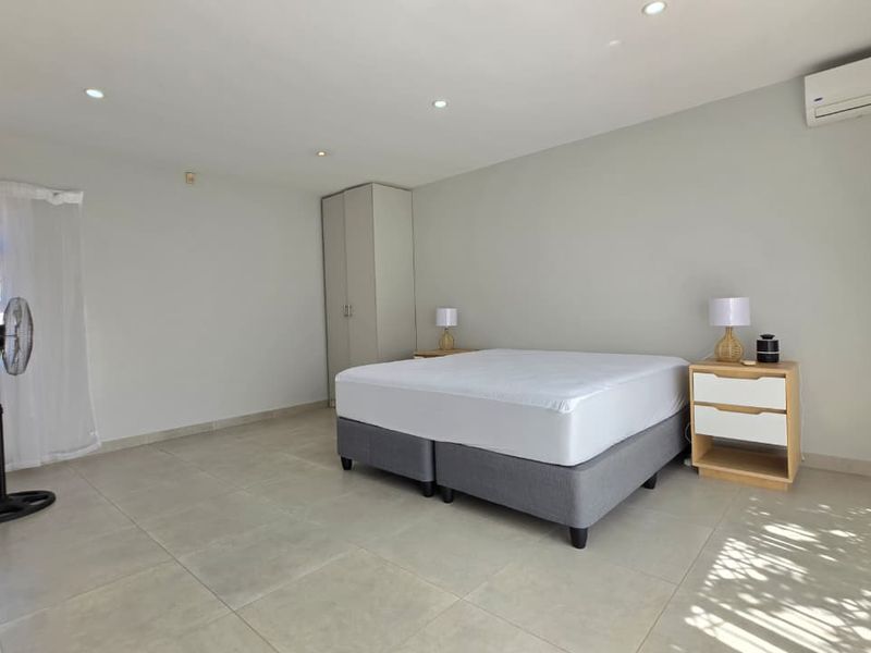 Spacious bedroom featuring neutral tiled flooring, recessed downlighting, a built-in wardrobe, and a wall-mounted split-system air conditioning unit.