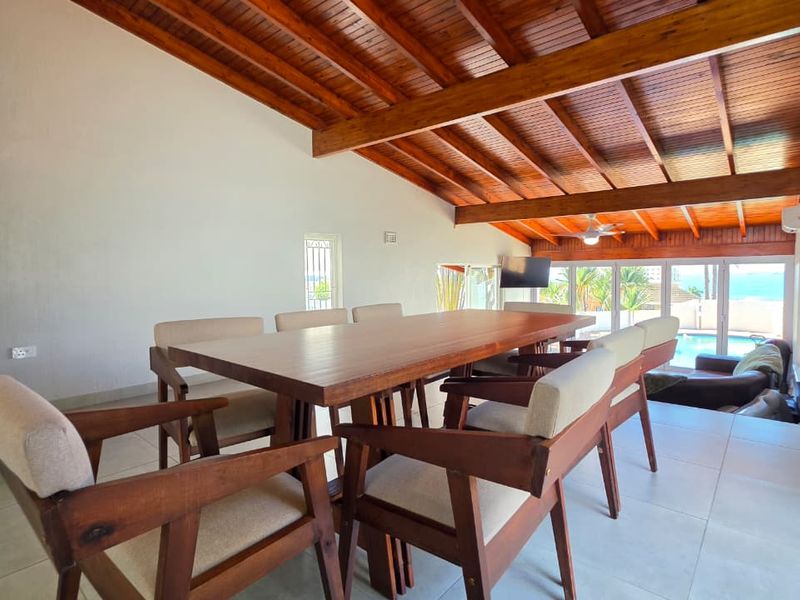Spacious dining area featuring a vaulted timber beam ceiling, large format floor tiles, and sliding glass doors opening to an outdoor pool area.