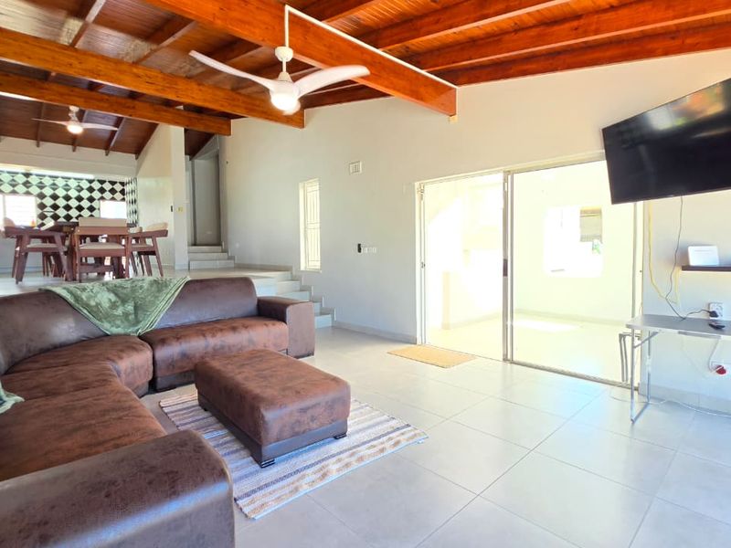 Spacious open-plan living area featuring exposed timber ceiling beams, tiled flooring, and seamless access to an outdoor patio through sliding glass doors.