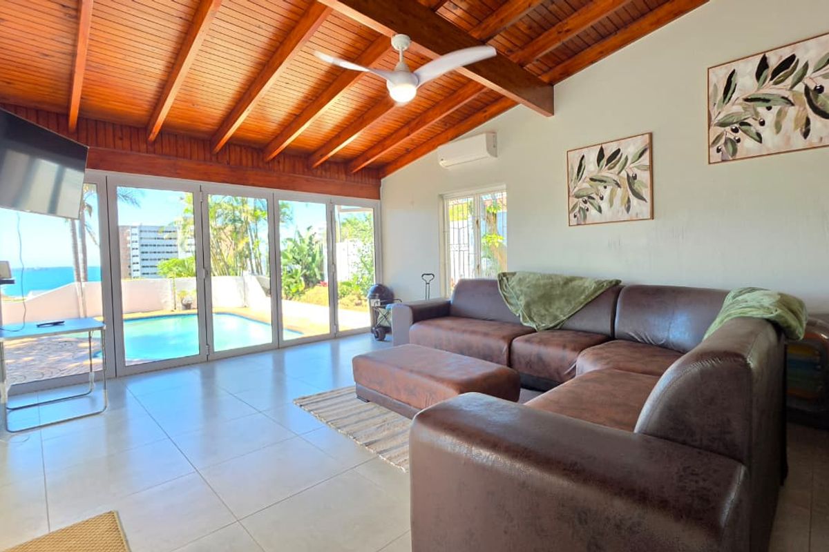 Spacious living room featuring exposed timber beam ceilings, tiled flooring, and large sliding glass doors providing direct access to the pool area.