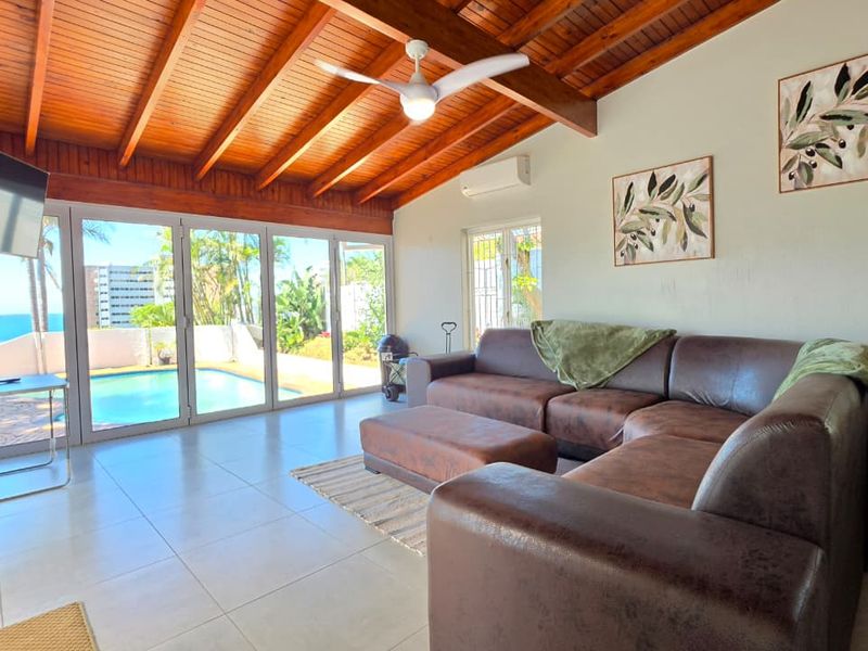 Spacious living room featuring exposed timber beam ceilings, tiled flooring, and large sliding glass doors providing direct access to the pool area.