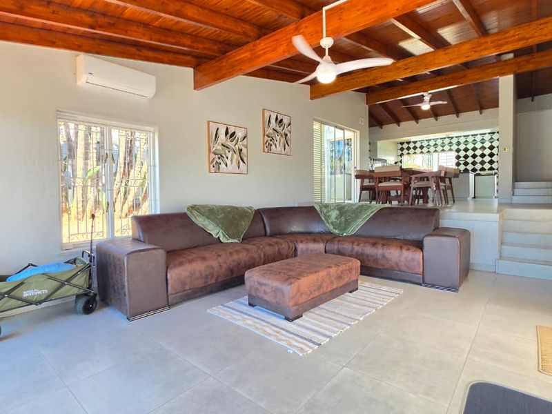 Spacious open-plan living area featuring exposed timber beam ceilings, tiled flooring, and a split-system air conditioner, flowing into a raised dining space.