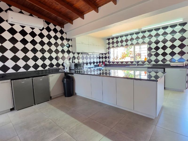 Spacious kitchen featuring modern white cabinetry, granite countertops, striking black and white checkered wall tiles, and exposed timber ceiling beams.