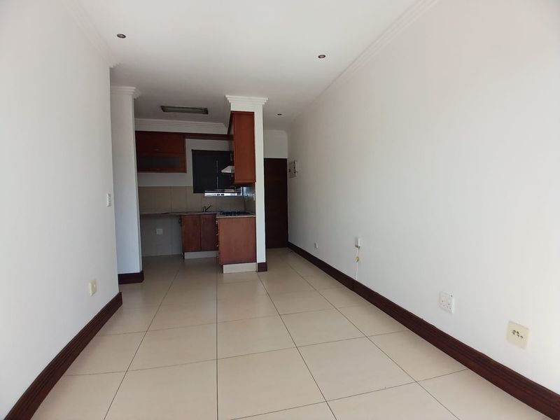 An open-plan living and kitchen area featuring tiled flooring, built-in wooden cabinetry, and a functional kitchen layout with integrated appliances.