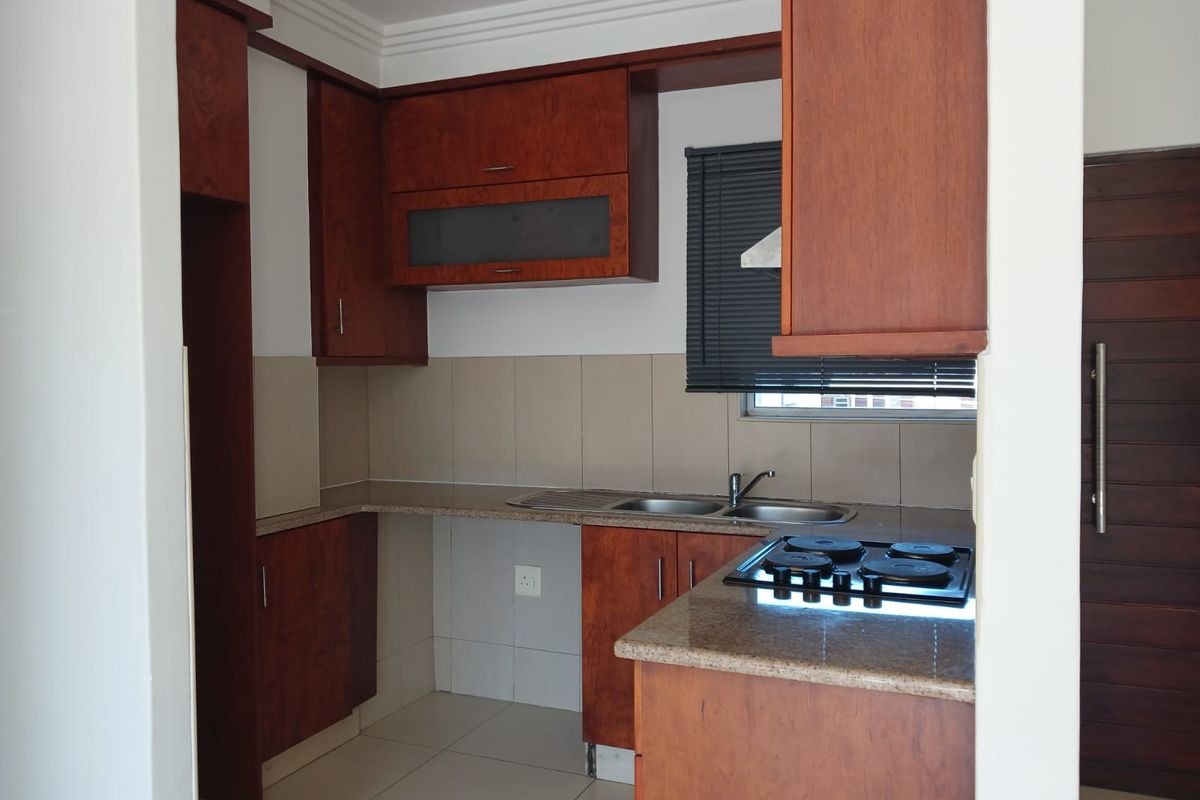 A functional kitchen featuring warm-toned wooden cabinetry, granite countertops, a built-in electric hob, and a stainless steel double sink with tiled backsplash.