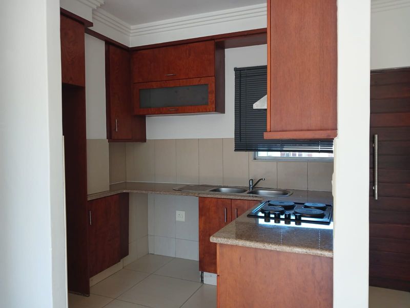 A functional kitchen featuring warm-toned wooden cabinetry, granite countertops, a built-in electric hob, and a stainless steel double sink with tiled backsplash.