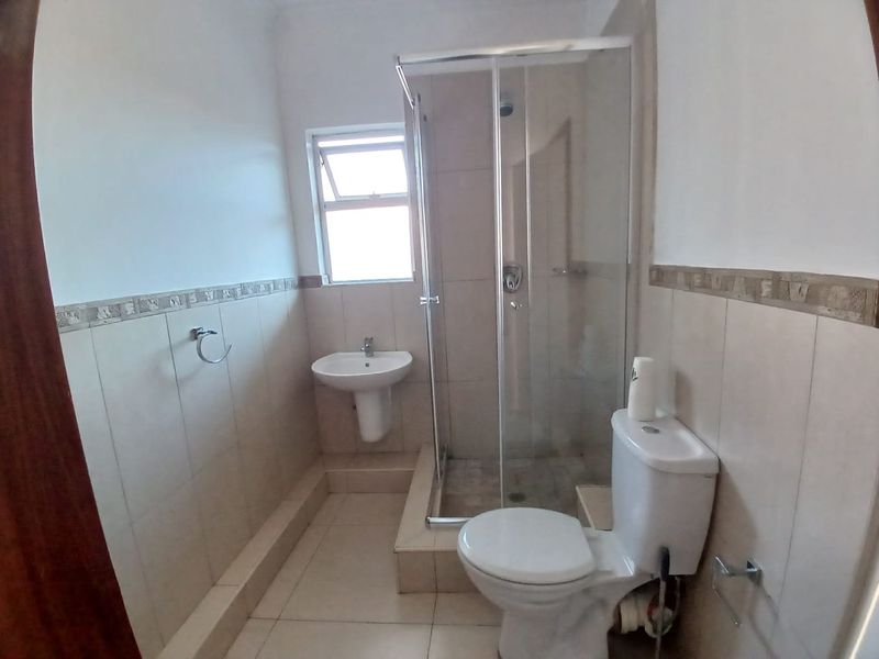 A functional bathroom featuring a pedestal washbasin, a glass-enclosed shower, and a standard toilet with neutral wall and floor tiling.