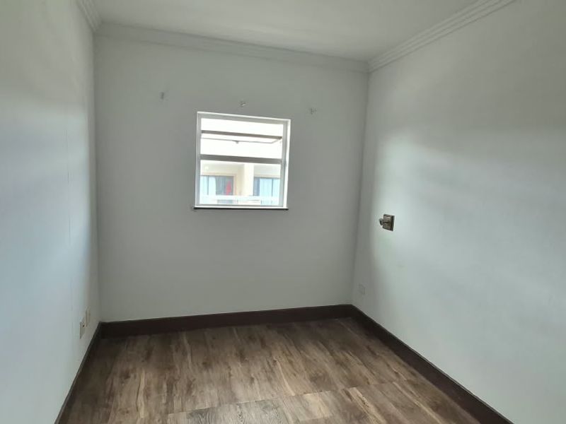 A clean, empty bedroom featuring laminate flooring, neutral walls, and a central window, providing a blank canvas for personalization.