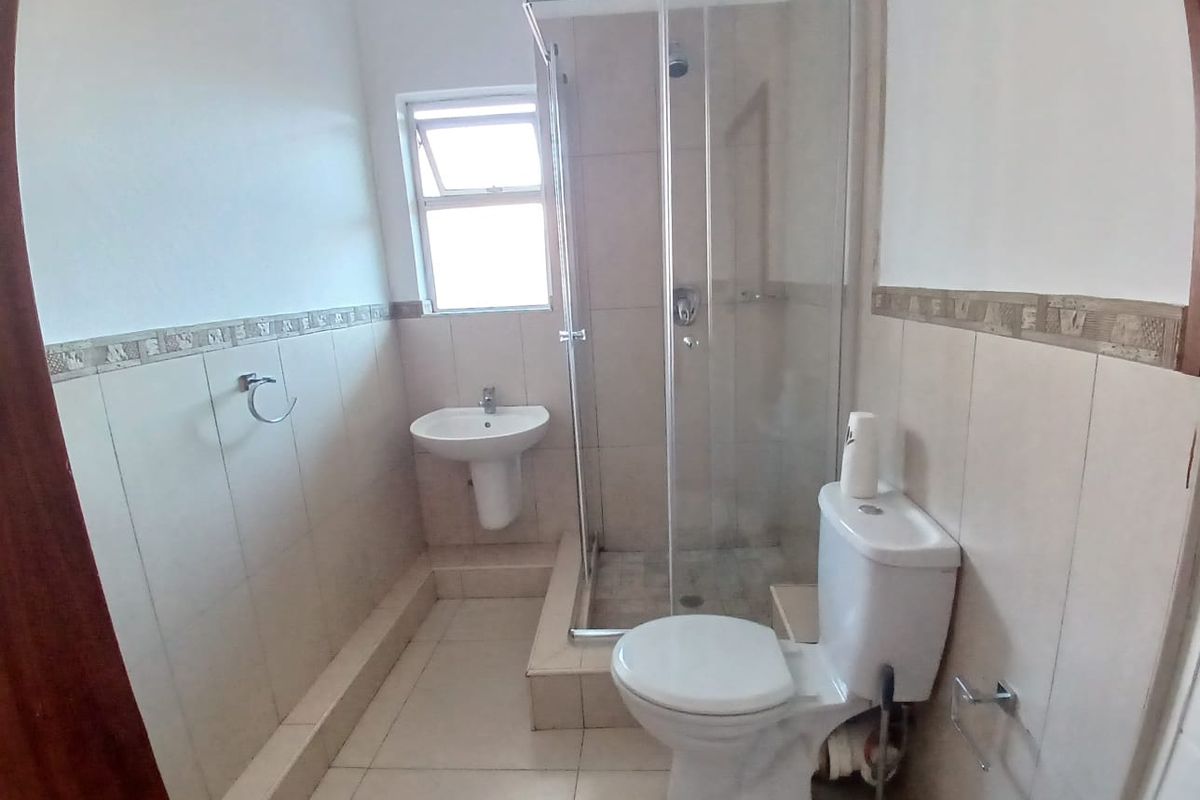 A functional bathroom featuring a shower enclosure, pedestal basin, and toilet with neutral wall and floor tiling.