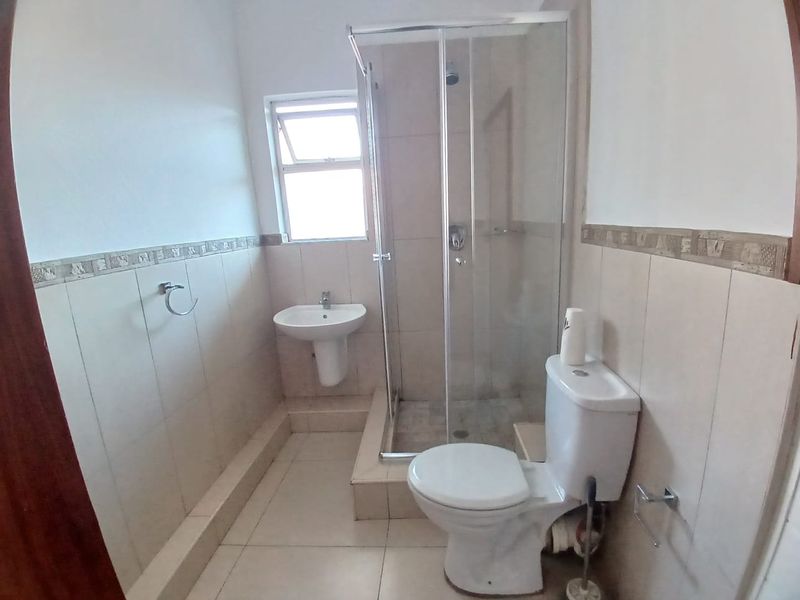 A functional bathroom featuring a shower enclosure, pedestal basin, and toilet with neutral wall and floor tiling.