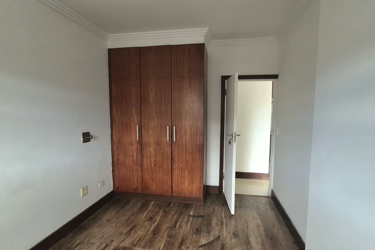 A clean, empty bedroom featuring laminate flooring, a built-in wooden wardrobe, and coved ceiling details, offering a neutral space ready for personalization.