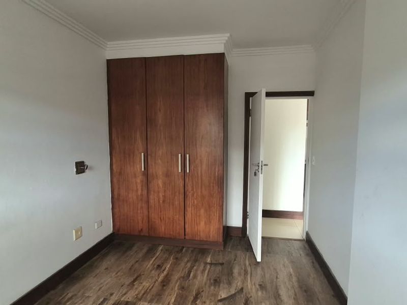 A clean, empty bedroom featuring laminate flooring, a built-in wooden wardrobe, and coved ceiling details, offering a neutral space ready for personalization.