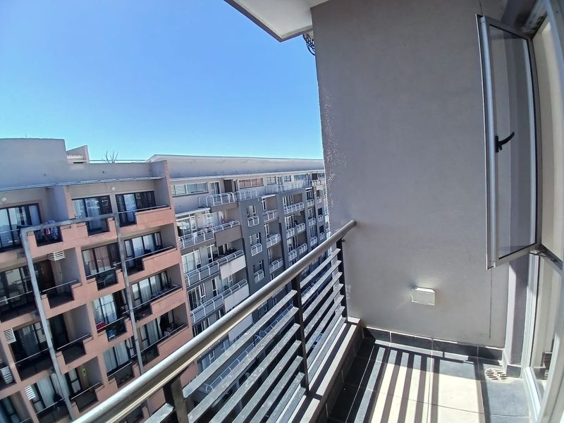 A clean, tiled balcony featuring a metal balustrade and an external wall light, offering an open view of the surrounding apartment complex.