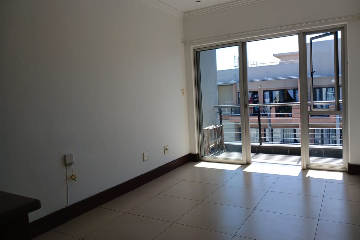 An empty, well-lit living area featuring neutral tiled flooring and a sliding glass door providing direct access to a private balcony.