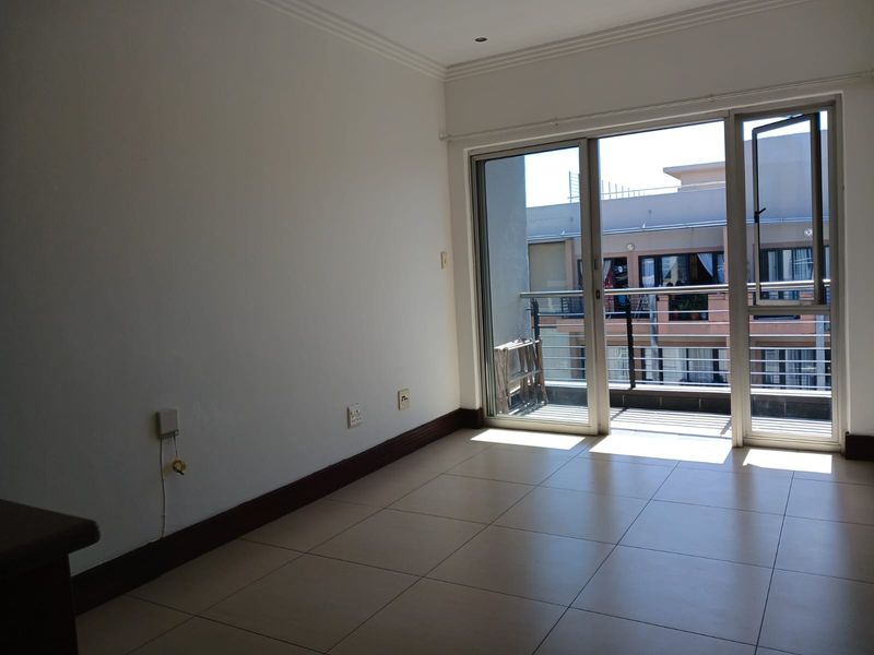An empty, well-lit living area featuring neutral tiled flooring and a sliding glass door providing direct access to a private balcony.