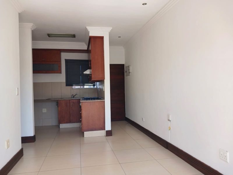 Open plan living area featuring tiled flooring and a compact kitchen with built-in cabinetry, hob, and extractor fan.
