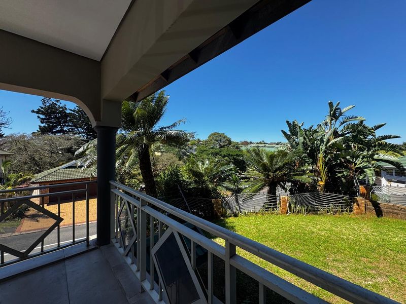 A covered balcony featuring tiled flooring and a metal balustrade, offering an elevated view over the garden and surrounding neighborhood.
