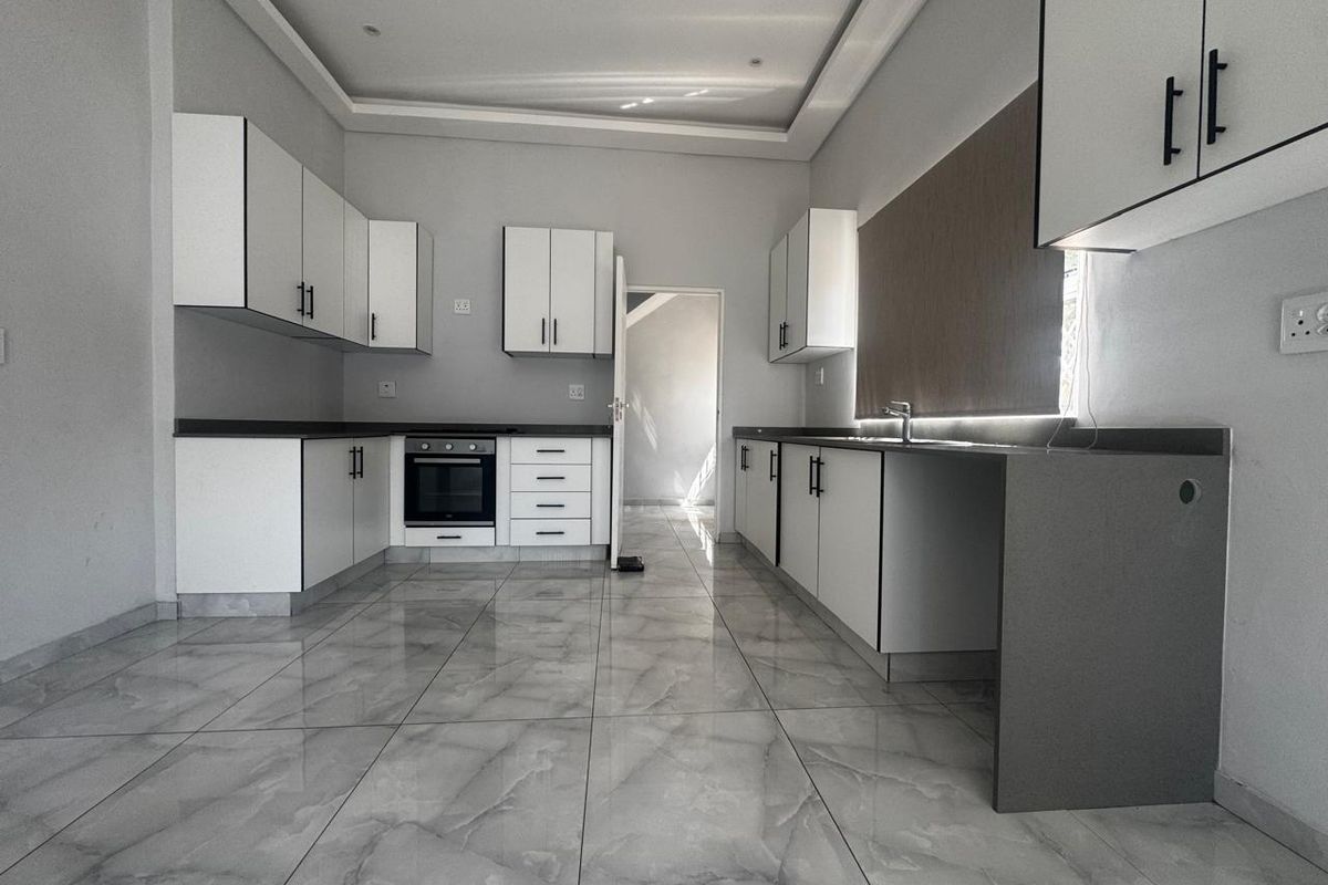 Modern, empty kitchen featuring white cabinetry, dark stone countertops, built-in oven, and large format grey marble-look floor tiles.