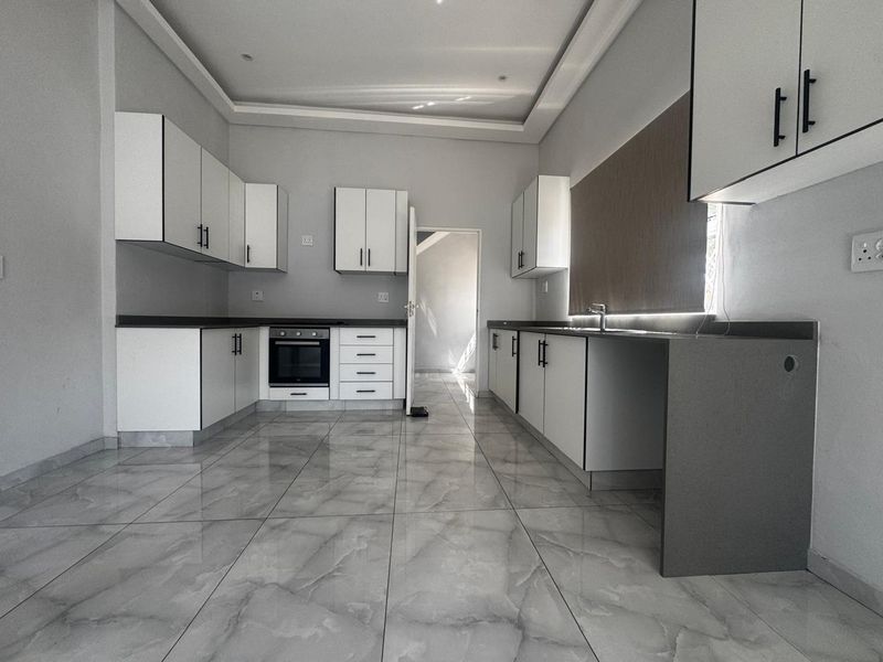 Modern, empty kitchen featuring white cabinetry, dark stone countertops, built-in oven, and large format grey marble-look floor tiles.