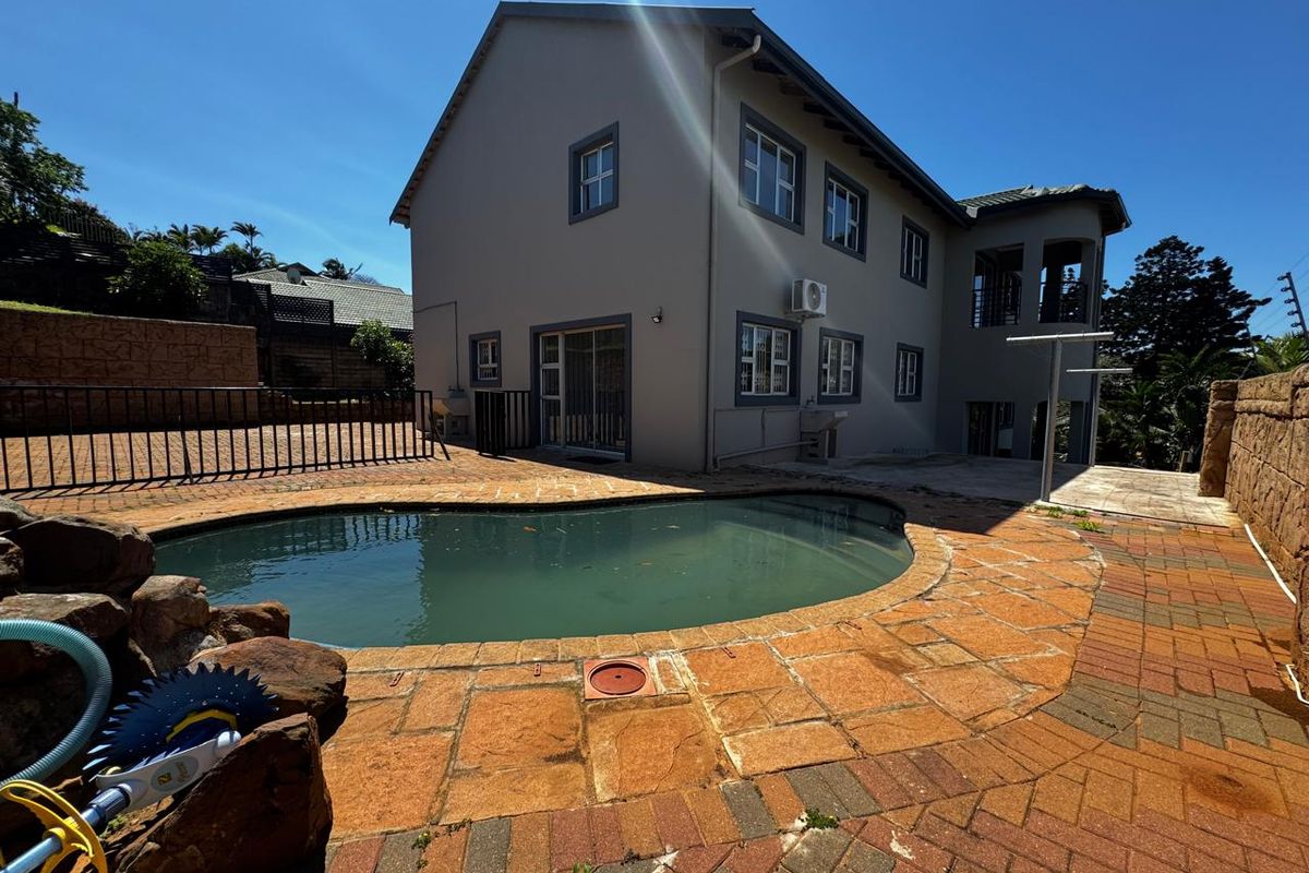 Rear exterior view of the house featuring a swimming pool, paved patio area, and multi-story building facade.