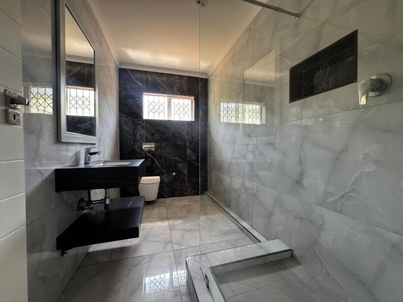 Modern bathroom featuring a walk-in shower with glass screen, recessed niche, wall-hung vanity, and contemporary marble-look tiling throughout.