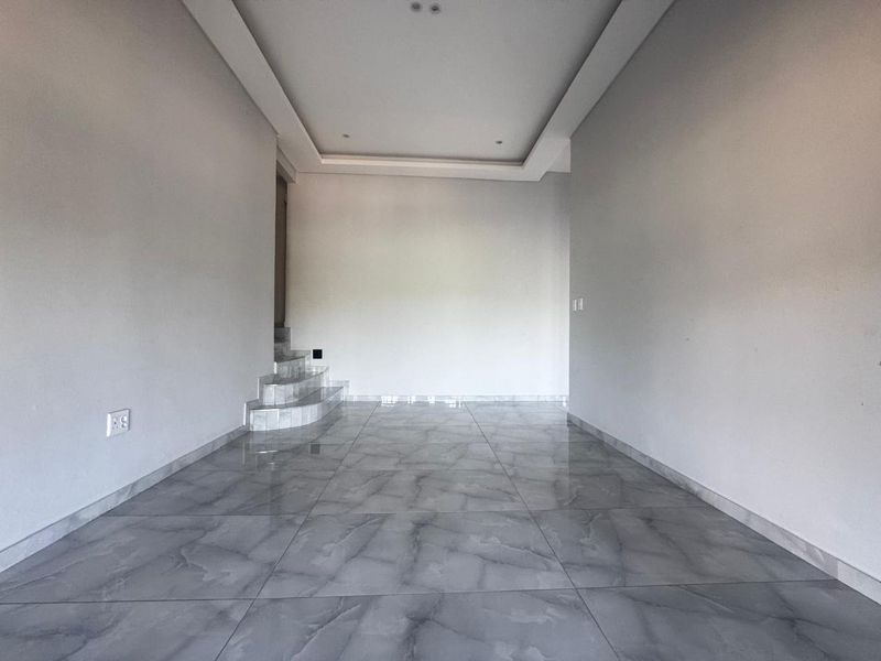 A spacious, empty living area featuring modern grey marble-look floor tiles, a recessed ceiling design, and a small internal staircase.