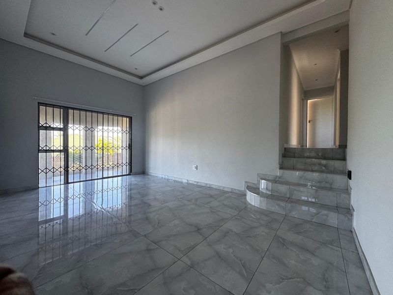 Spacious, empty living area featuring modern grey tiled flooring, a recessed ceiling, and a sliding door with a security gate leading outdoors.