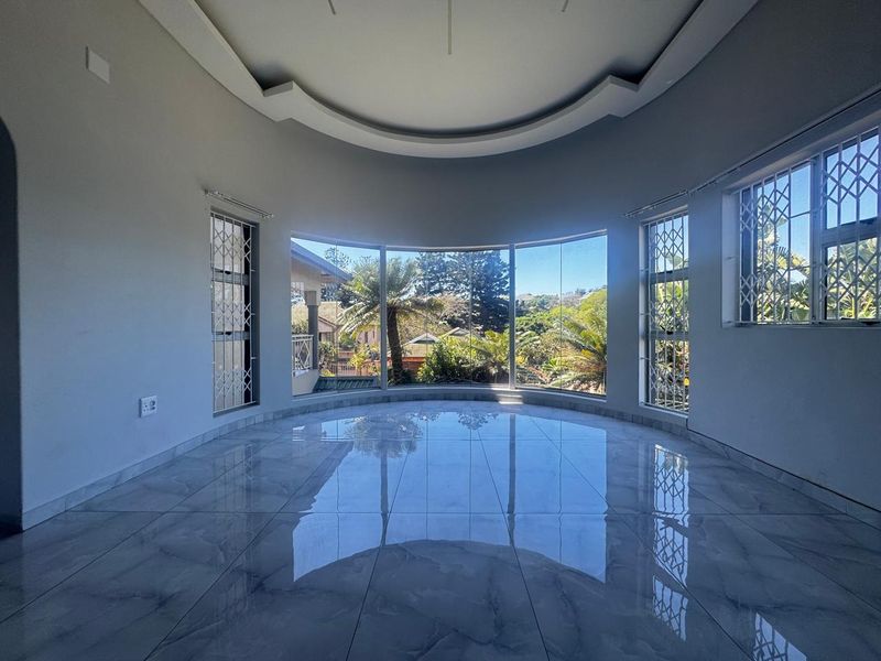 Spacious living area featuring polished porcelain tiles, a decorative recessed ceiling, and large windows offering natural light and garden views.