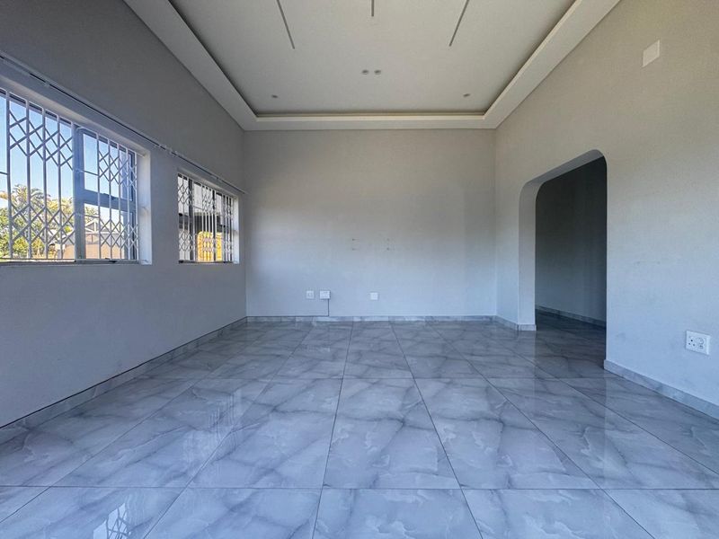 A bright, empty living room featuring modern grey tiled flooring, a recessed ceiling design, and security bars on the windows.
