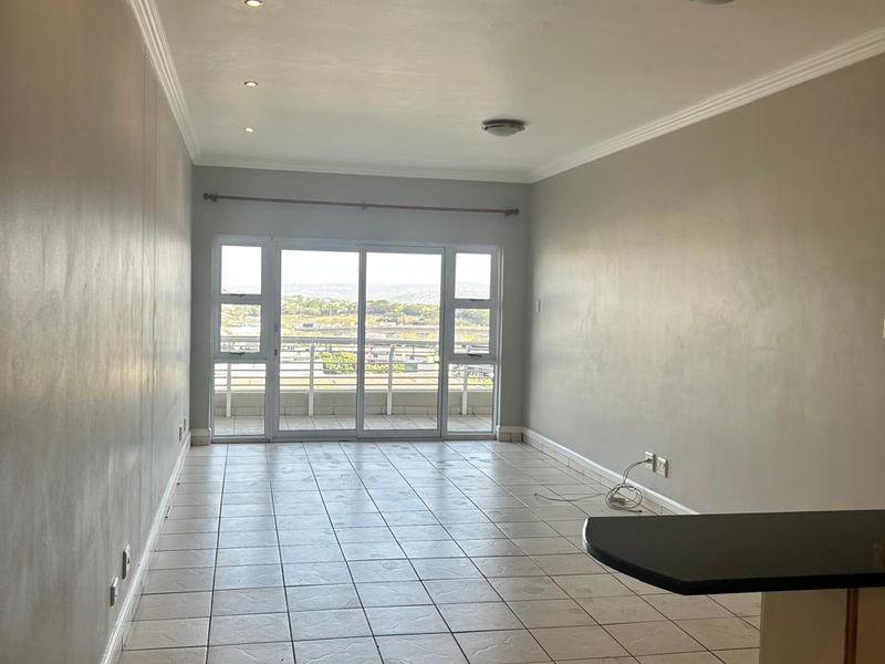 Spacious open-plan living area featuring tiled floors, recessed lighting, and sliding glass doors leading to a balcony with scenic views.