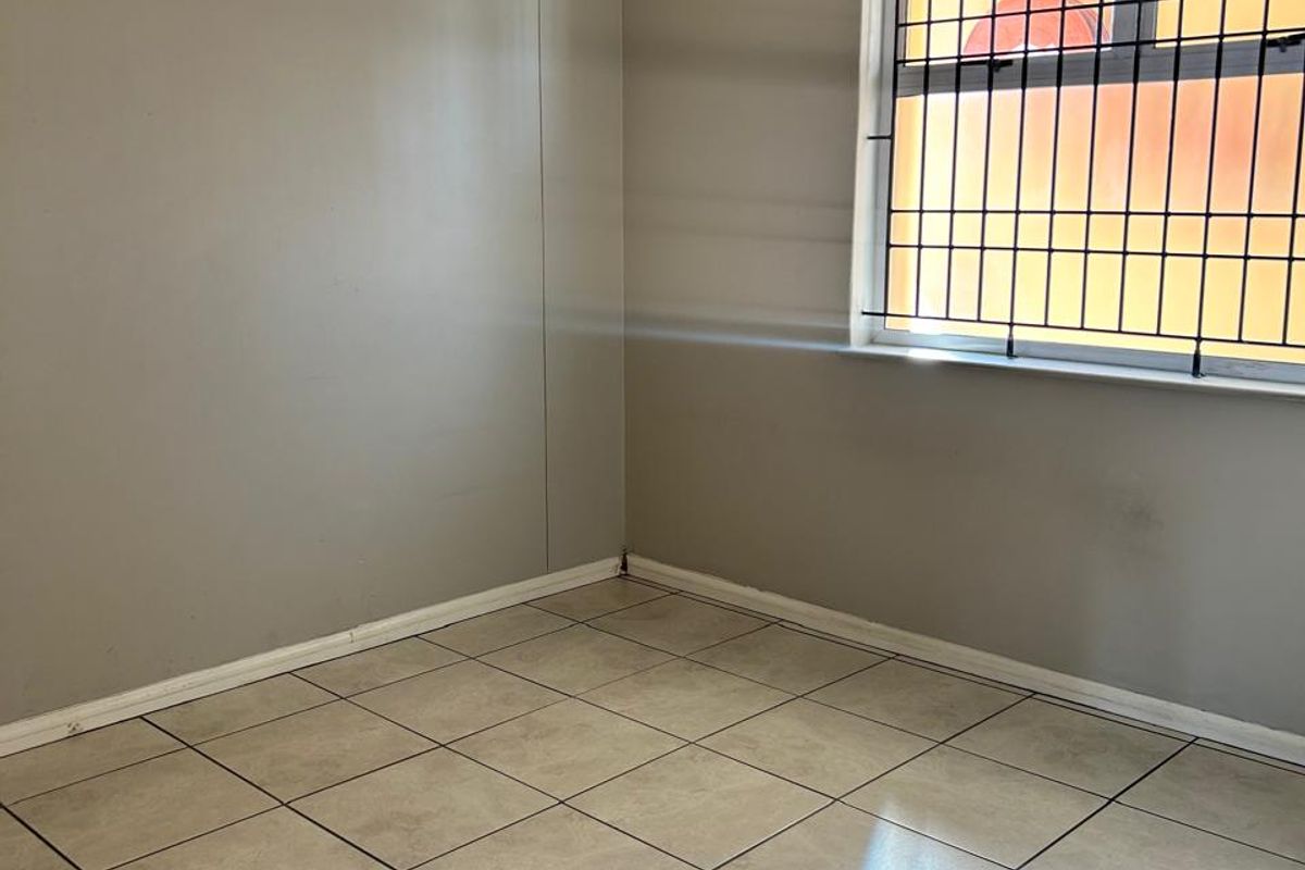 An empty bedroom featuring neutral tiled flooring, security bars on the window, and simple wall finishes, ready for personalization.